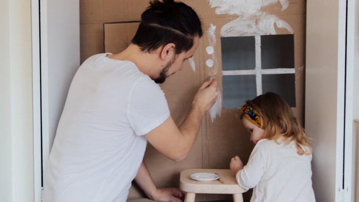 man in white t shirt and brown pants painting cardboard house